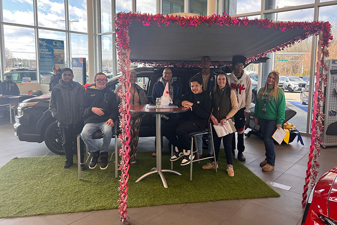 Group of workers and kids at event in front of car